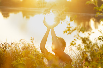 woman hands in mudra like in the palm of hands, at sunset  on the lake in nature - obrazy, fototapety, plakaty