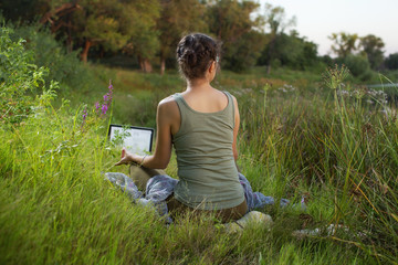 woman practicing yoga asanas and meditation in nature  at sunset with laptop