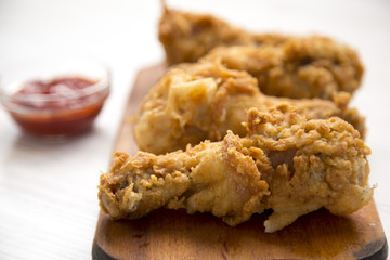 Fried chicken drumsticks with sauce on wooden board over white wooden surface, side view. Close-up.