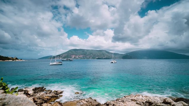Beautiful 4k cloudscape near Fiskardo, Kefalonia, Ionian islands, Greece. Flowing clouds over Crystal clear transparent Mediterranean sea water. White catamaran yacht drifting in open sea. Time lapse