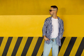 fashion guy in a striped shirt is standing near a yellow parking wall