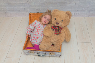 the girl, child with bear and suitcase on white brick wall background