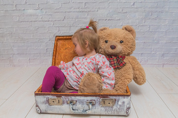 the girl, child with bear and suitcase on white brick wall background