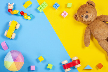 Baby kids toys frame with teddy bear, wooden toy car, colorful bricks on blue and yellow background. Top view