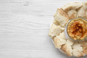 Bowl of Hummus with chickpeas, paprika, olive oil and pita bread on white plate over white wooden surface, top view. From above, overhead, flat lay. Copy space.