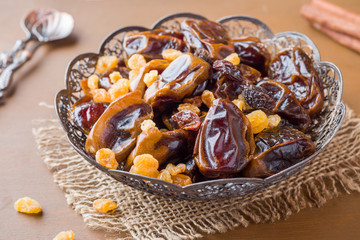 Oriental sweets, dried fruit dates and raisins, cinnamon and star anise in a plate on a wooden background.