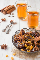 Oriental sweets, dried fruit dates and raisins, cinnamon and star anise in a plate. Turkish tea in glasses on a wooden background.