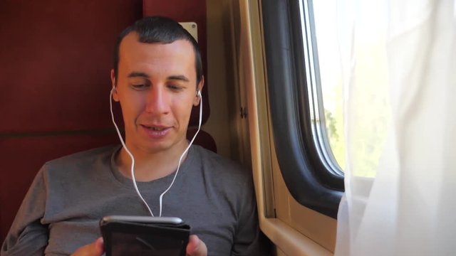 man listening to the music on the train rail car coupe compartment travel. slow motion video. man with a smartphone at the window of a train in a car travel internet social media web. man train wagon