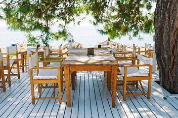 Fototapeta na wymiar Restaurant with tables on a snow-white terrace overlooking the sea under pine branches. Rest on the sea