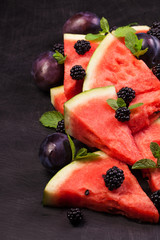 Sliced watermelon with blackberries and mint leaves on black backgroung. Healthy vegetarian food
