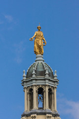 Fototapeta premium Edinburgh, Scotland, UK - June 14, 2012: Golden statue of female representing Victory on top of tower of the Mound building against blue sky. Seen from Royal Mile.