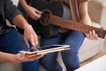Man showing sheet music on tablet computer to his girlfriend who is playing guitar