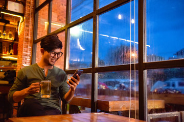 Young Asian business casual drink beer. Check out the relaxed application on smart phones. People use smartphones and surf the Internet in the beer shop.