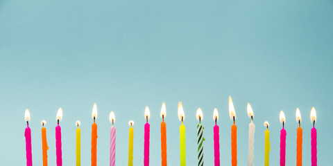Set of many different color shape and pattern birthday candles burning in long row, isolated on...