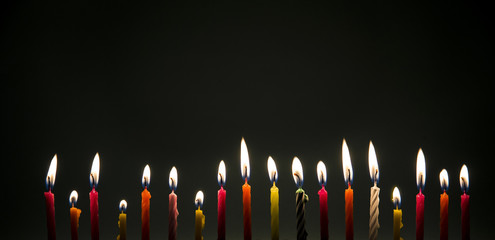 Set of many different color shape and pattern birthday candles burning in long row in dark isolated on black. Happy Birthday card design concept. 