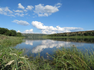 Naklejka premium Picturesque landscape with green valley, river, hills and blue sky. White clouds are reflected in the water surface