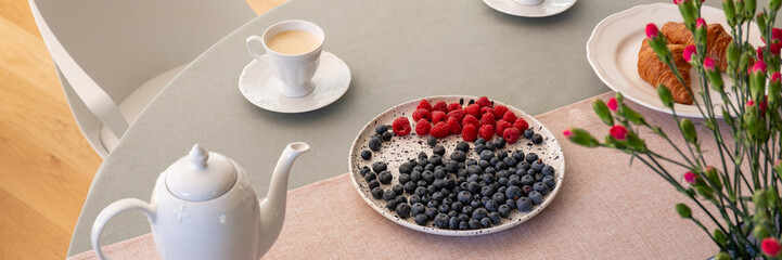 Fototapeta na wymiar Panorama of fruits on plate, kettle and cup of coffee on table in restaurant interior. Real photo