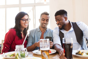 leisure, technology and people concept - group of happy international friends with smartphone at restaurant table