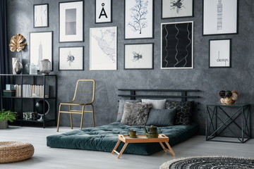 Gold chair next to green mattress and wooden tray in bedroom interior with gallery and pouf. Real...