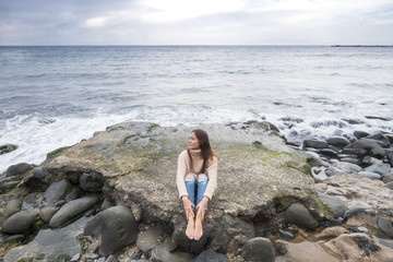 Fototapeta na wymiar lonely beautiful young woman listen music and relaxing with meditation and concentration sitting on a rock with ocean and horizon and nobody in background. enjoying loneliness concept