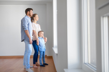 family, people and real estate concept - happy mother, father and little son looking through window at new home or apartment