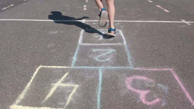 Boy jumps playing hopscotch in the street. Close-up legs.