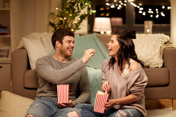 hygge, leisure and people concept - happy couple eating popcorn at home