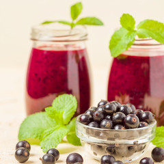 Currant smoothie decorated with fresh green mint leaves and raw ripe berries on yellow pastel background.