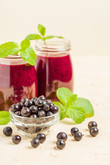 Currant smoothie decorated with fresh green mint leaves and raw ripe berries on yellow pastel background.