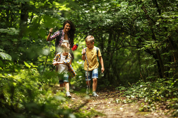 Mother and her little sons hiking trough forest. They're learning about nature.	