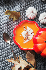 Fall pumpkin cream soup with seeds in red ceramic bowl.