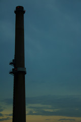 Tall Concrete Industrial Factory Smoke Stack Environmental Pollution Tower with Glowing Bright Red Flashing Lights Against Dark Blue Yellow Cloudy Twilight Evening Sky