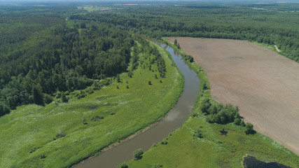 Fototapeta premium Aerial view summer landscape, river among trees, farmlands. Countryside with forest, the banks river covered with greenery.