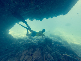 Male diver swimming through natural underwater tunnel.