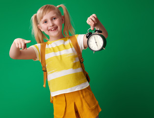 happy pupil pointing at alarm clock on green background