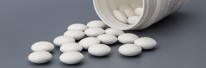 White round pills scattered from a white jar.