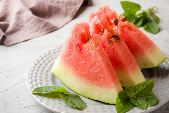 Watermelon sliced on a plate with mint leaves on a wooden background.