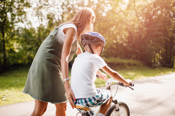 Mom and little boy learning to ride bicycle park having fun together