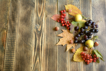 Fototapeta na wymiar Autumn composition of colorful leaves red berries, apple, dried oranges and nuts on a wooden background with autumn concept copy space