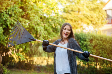 Smiling young woman with garden hose watering her home backyard with flowers, plants and vegetation. Gardening as hobby and leisure concept.