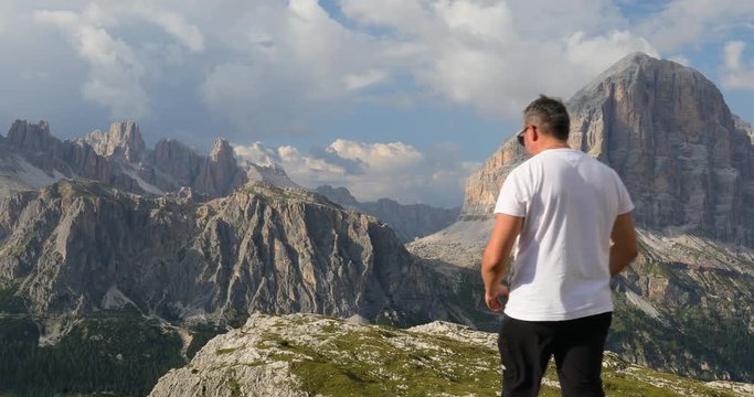 Dolomites, Tofana de Rozes. Alpine landscape. A man approaches and takes a picture of the landscape using his cell phone. In the background the dolomite rocks of the Italian alpine mountains.