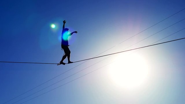 Silhouette of a man walking on a rope on the background of the sun. Rope-walker.