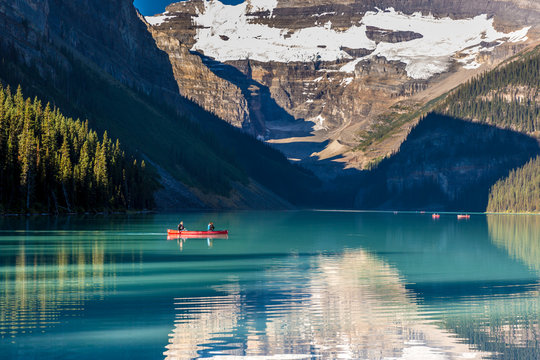 Banff, Canada - Ago 19th 2017 - Tourists doing kayak and enjoying the amazing scenario of lake Moraine, early morning light, glacial at the background, blue sky in summer time Banff.