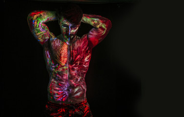 Young man painted in fluorescent paint on face and muscular torso, in studio shot with UV light