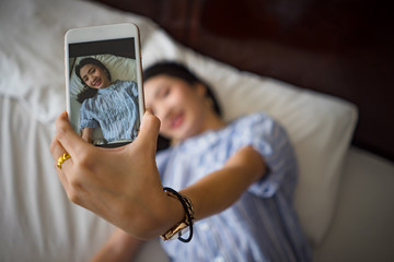 young happy woman taking  selfie with mobile phone in bedroom morning..Asian cute girl lying on bed...