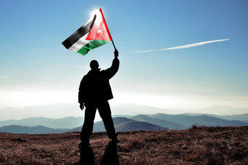 Successful silhouette man winner waving Jordan flag on top of the mountain peak