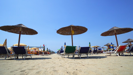 Summer beach resort bar lounge area with wooden easy chairs and straw parasols lined up next to the sea water
