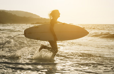 Woman with surfboard standing on wet sandy beach at the ocean.