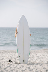 Anonymous person hugging while surfboard while standing on background of waving sea