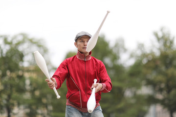 A man in a cap juggles with clubs on the street of a European city